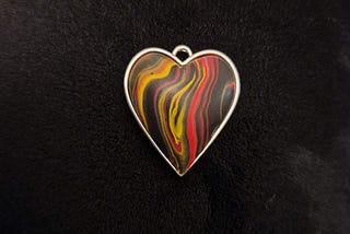 Picture of a coloured heart with black, red, yellow and orange swirls on black background.