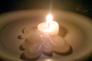 a small lit candle on a plate with wax oozing out in the dark