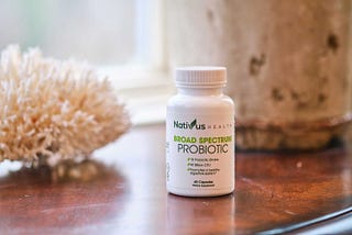 A bottle of Nativus Health Broad Spectrum Probiotic on a table next to a window with beautiful light coming in