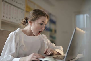 A young woman staring in shock at her laptop screen.