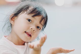 Photo of a young girl holding her hands out looking quizzical