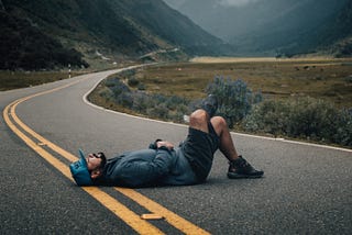 A man naps in the middle of the street with one leg crossed over the other.