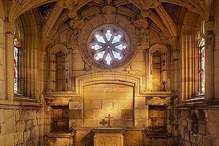 An old stone building with a star-shaped window and an altar on which a small cross is placed.