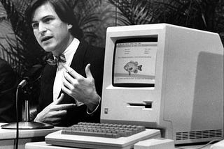 A young Steve Jobs wearing a non-customary blazer and bow tie introduces the original Macintosh in 1984.
