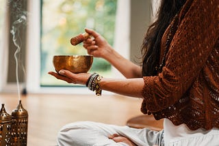 Woman playing a Tibetan sound bowl and meditating.