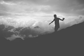 silhouette of man balancing on sloped hillside with cloudy sky in background