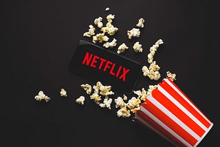 A mobile screen is displaying Netflix and popcorn is spilled around the device.