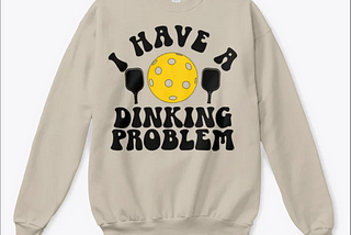 White sweatshirt reading “I have a dinking problem” with an image of a pickleball and paddles.