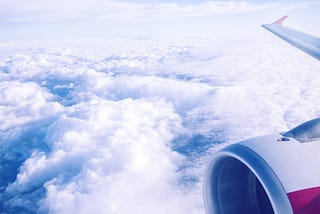Outside view of a passenger plane’s wing and engine over clouds