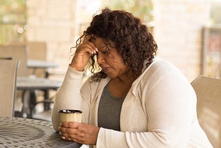 Talk2Me Therapy — Over-functioning — Black woman — Woman of Colour — holding a coffee looking stressed with her hand on her head