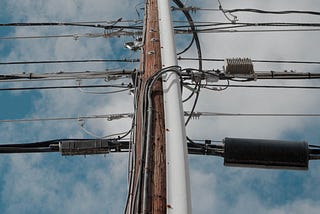 A telephone pole with a dozen wires running from either side of it, viewed upward from the base of the pole.