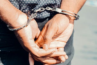 Picture of a man with his hands behind his back, wearing handcuffs.