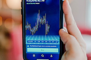 Person holding a smartphone with a cryptocurrency graph displayed on the screen