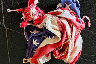 Contorted and worn American flag on a black background with white streaks.