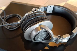 A pair of Audio-Technica M50X headphones in gray sits on a closed laptop. The cord is attached, and loosely sitting to the left side of the frame.