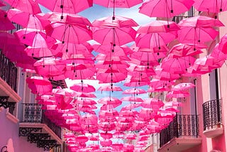 pink umbrellas hanging between two pink buildings