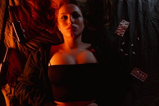 A woman on a bed in the dark with bottles and pills around her.