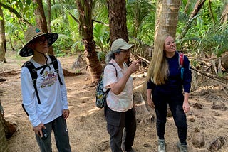 Ruth Utzurrum (center) on Island Dano, Guam, standing with Jay Gutierrez (left), Chief of Guam’s Division of Aquatic and Wildlife Resources (DAWR), and Lauren Thompson (right), wildlife biologist for DAWR. They are standing in a jungle with palm trees in the backdrop.