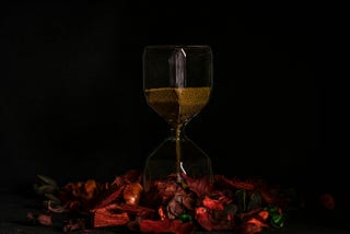 An hourglass on a bed of red rose petals, set in a black background.