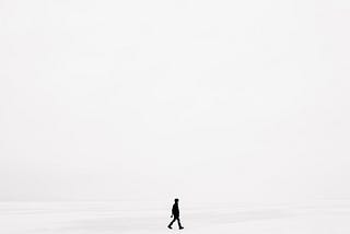 A dark silhouette walking through a vast empty white space.