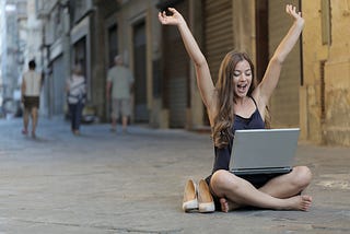 A woman enjoying watching her laptop while sitting on the floor.