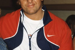 A smiling Owen Hart wearing a WWF hat while meeting fans.