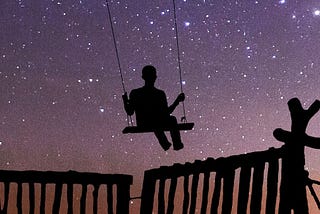 Silhouette of a person in a swing against a starry evening sky