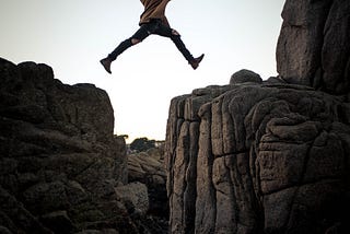 person jumping over a large gap between two mountain ledges