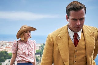 A screenshot from the 2020 film Rebecca. Lily James stands in the background Armie Hammer stands in the foreground.