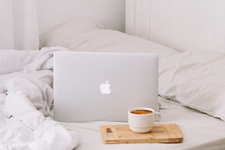 A laptop and a cup of coffee on a white bed.