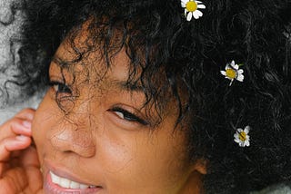 A Black girl with flowers in her hair smiles.