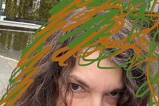 Close up selfie photo of the top half of my head, just showing my eyes, and lots of green and brown scribble on my hair and around my head.