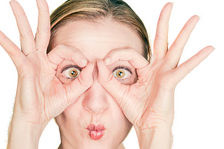 Close-up of woman’s face as she makes imaginary glasses over her eyes with her thumbs and forefingers.