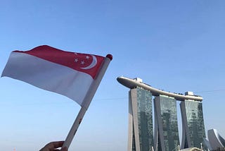 a hand held falg of Singapore waving against the backdrop of the Marina Bay Sands Hotel