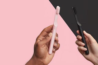 Promotional photo from Quip of two hands holding two different Quip toothbrushes. One in pink and one in black.