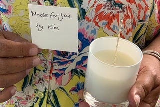 A woman holds up a newly-made candle with a note that says “Made for you by Kim.”