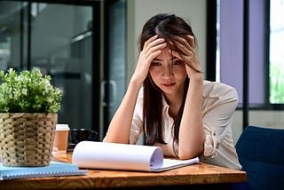 A stressed young woman holds her head while looking at financial information.