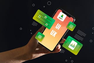 Imagem com fundo preto que contém uma mão segurando um smartphone. Na tela do smartphone é possível ler as siglas UI e UX e também contém algumas ilustração com fundo verde e gráficos “saindo” da tela do smartphone.