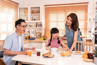 A father, mother, and daughter about to share a happy meal together, smiling and enjoying each other’s company at the dining table by Buhairi Rifqa Moustafid