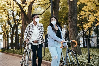 Young multiethnic friends walking with bikes near trees