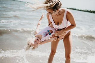 Woman and daughter playing in the waves at the beach.