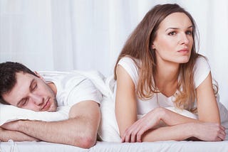 couple in bed man sleeping pensive woman