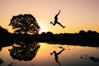 Someone leaping high above a body of water, at sunset. Photo by @kidcircus on Unsplash