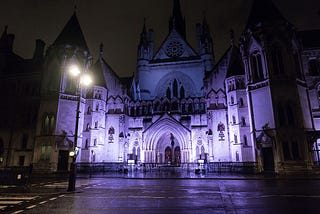 A nighttime photograph of the Royal Courts of Justice in London, UK