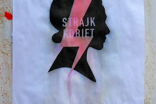 A flyer hangs on a wall in Sanok, Poland, October 2020. On a white background, a woman’s silhouette with a bright lightning bolt and the words, STRAJK KOBIET / WOMEN’S STRIKE