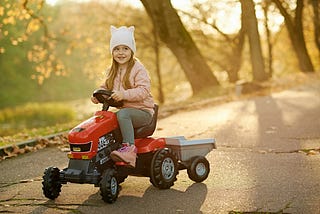 Girl riding a plastic tractor on a path in Autumn