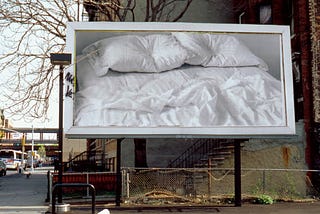 Photo of billboard with a picture of bed featuring two pillows with indentations where heads would have been.