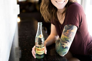 A woman with tattoos drinking a sparkling water