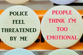 Two pin buttons. One says, “Police feel threatened by me”. The other says, “People think I’m too emotional”.