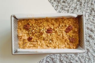 A carrot cake ready to be baked with a sprinkle of granola and 5 pecans.